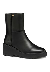 Bottine en cuir noir avec semelle compensée, bout rond et petit bouton décoratif en or près du bord supérieur.