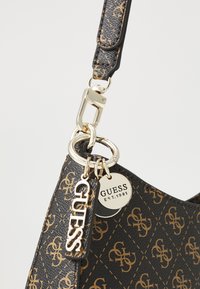 Fekete szintetikus kézitáska monogramos mintázattal, aranyszínű fémalkatrészekkel és "GUESS EST.1981" logós charm-mal. Állítható pánt tartozik hozzá.