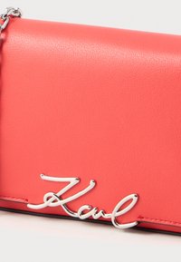 Koraļļu ādas soma ar sudraba ķēdes siksnu un spīdīgu sudraba "Karl" logo detaļu priekšējā atloka.