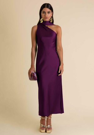 Abito in satin viola con design a spalla unica, spacco laterale e lunghezza fino al pavimento. Indossato con tacchi a piattaforma dorati e una pochette trasparente con gemme.
