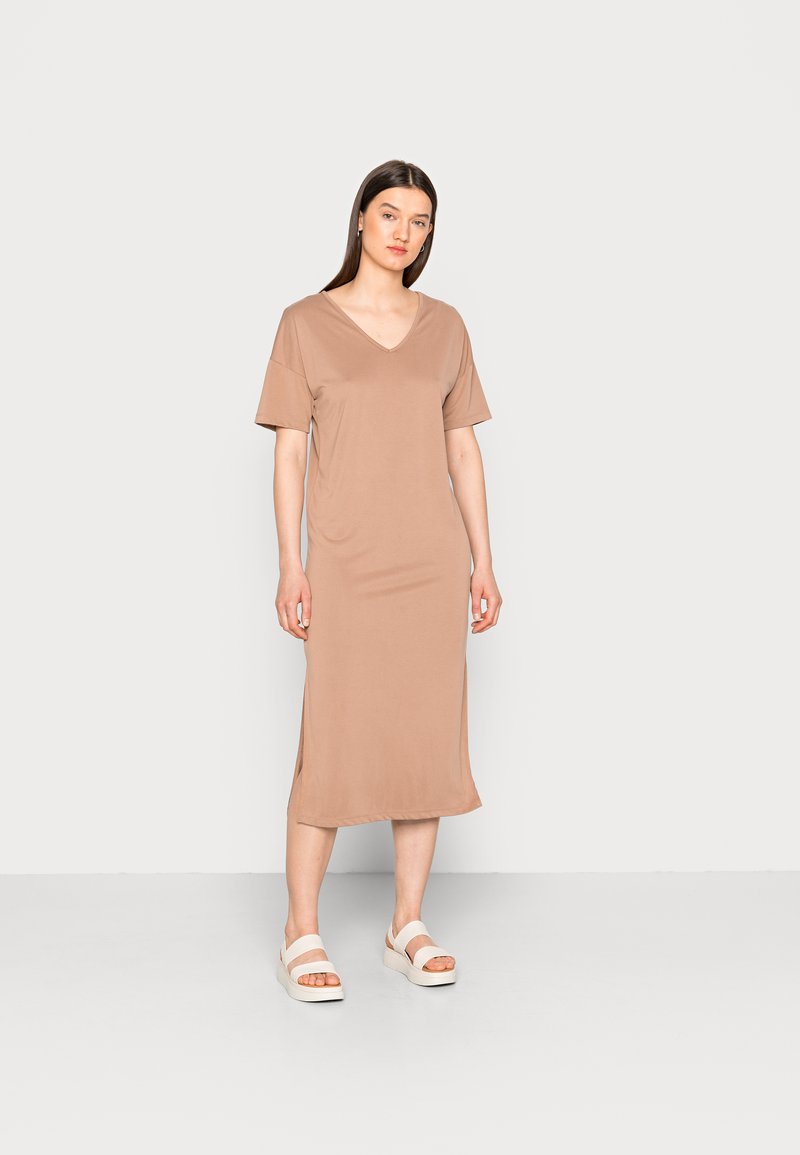 Vestido de mangas curtas em V, na cor castanho claro, feito de um tecido suave com fendas laterais. Combinado com sandálias de plataforma brancas.