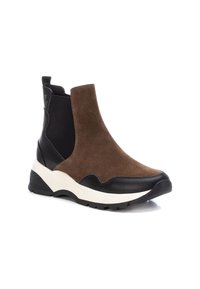 Botas Chelsea de ante marrón con paneles laterales elásticos negros y un tacón negro texturizado. Cuenta con una suela gruesa blanca para mayor soporte.