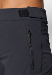 Crne sportske hlače od glatkog, rastezljivog materijala, s bočnim džepom sa zipom i podesivim čičak pojasom za sigurno prianjanje.