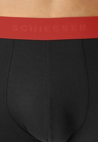 Sorte boxer briefs i sort med en glat tekstur og et rødt elastisk bælte, der har ordet "SCHIESSER" i diskret skrift.