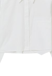 Camicia bianca con colletto a ribatti, pattina frontale, taschino singolo sul petto e orlo leggermente curvato. Realizzata in tessuto liscio.