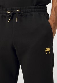 Mustat verkkarit, jotka on valmistettu pehmeästä kankaasta, sisältävät nyöritettävän vyötärön kullanvärisillä yksityiskohdilla, sekä kultaisen kobralogon vasemmassa reisissä.