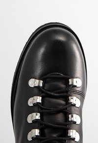 Botte en cuir noir à bout arrondi avec des lacets noirs passant à travers six paires d'œillets métalliques argentés.