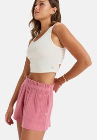 Vit kortad linne med texturerad tyg, kombinerat med rosa veckade shorts med elastisk midja och en liten accentknapp.