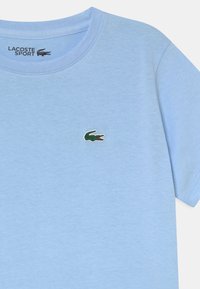 T-shirt en coton bleu clair avec un col rond et des manches courtes. Présente un petit logo de crocodile vert sur la poitrine gauche.