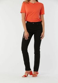 T-shirt orange à manches courtes associé à un jean slim noir et des sandales à talons rouges avec une bride texturée et un talon bloc.