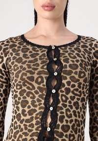 Top leopard stampato in tessuto a coste marrone e nero, con bordo in pizzo nero a ondine e sei bottoni bianchi sul davanti.