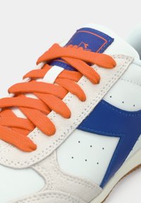 Λευκό δερμάτινο αθλητικό παπούτσι με πορτοκαλί κορδόνια, μπλε λεπτομέρειες και υφασμένη σουέτ λεπτομέρεια. Διαθέτει οπές για αερισμό και καουτσούκ σόλα.