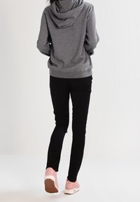 Grå huvtröja med snören, svarta tajta byxor och rosa sneakers. Huvtröjan har en mjuk textur och en kenguruficka.