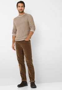 Pantaloni corduroy marroni abbinati a un maglione leggero marrone testurizzato. L'outfit include stivali alla caviglia marroni scuri e ha una vestibilità rilassata.
