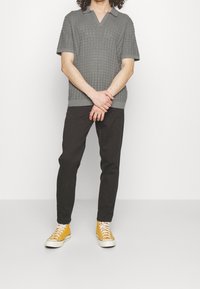 Grå strikket poloshirt med korte ærmer og V-hals, kombineret med sorte bukser og gule sneakers. Tekstureret design over det hele.