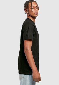 Black cotton t-shirt with short sleeves and a classic crew neck, displayed on a model in profile against a neutral background.