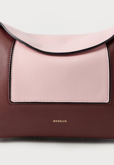 Sac à main en cuir avec un rabat rose courbé sur un panneau rectangulaire rose clair sur un corps brun foncé, logo doré "WANDLER" centré en dessous.