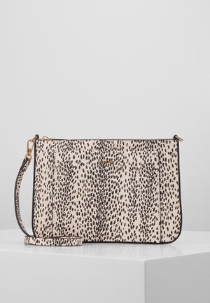 Beige crossbodytas met onregelmatige zwarte stippen, gouden rits en afneembare riem, geplaatst op een wit voetstuk tegen een lichtgrijze achtergrond.
