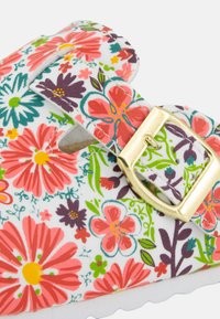Chaussure à motif floral avec fond blanc, ornée de fleurs roses, violettes et vertes. Accent de boucle dorée et semelle rembourrée.