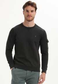 Zwarte sweatshirt met een ronde hals, lange mouwen en een patchzak op de linkerarm. Gemaakt van een glad materiaal met een aansluitend ontwerp.