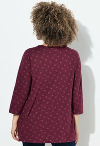 Tunic bordeaux con maniche a tre quarti, caratterizzata da un sottile motivo a tutto campo di piccole forme, realizzata in un tessuto leggero e testurizzato.
