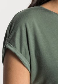 Grön kortärmad topp gjord av mjukt, lättviktsmaterial. Har rullade ärmar och en avslappnad passform som framhäver en jämn textur.