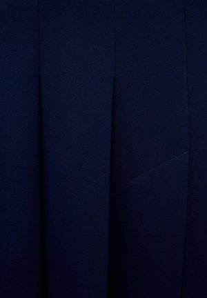 Mørkeblå stof med en glat tekstur har folder og en diskret syet lomme. Designet fremhæver rene linjer og minimale detaljer.