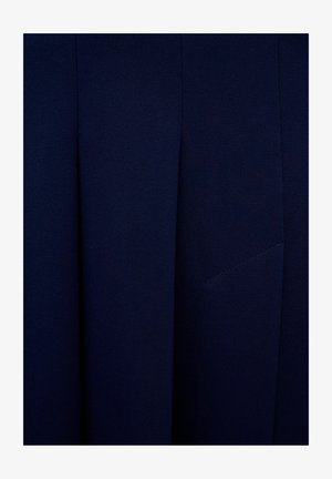 Granatowy materiał o gładkiej fakturze, z plisami i dyskretną, wszytą kieszenią. Projekt podkreśla czyste linie i minimalizm.