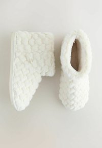 Witte, pluizige slippers met een getextureerd, gewatteerd patroon. Zacht imitatiesuede materiaal met een gevoerde binnenkant en een witte zool.