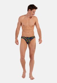 Schwimmbriefe aus schwarzem Stoff mit einem bunten abstrakten Muster von Formen. Das Design umfasst einen niedrig geschnittenen Schnitt und eine glatte Textur.
