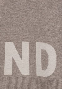 Beige Strickpullover mit großen weißen Buchstaben "ND" auf der Vorderseite. Weiche Textur mit geripptem Saum.