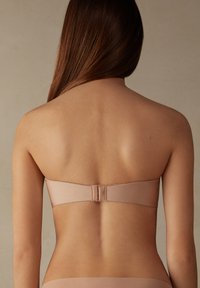 Beige strapless bh met een naadloos ontwerp, zachte textuur en brede band, met een haaksluiting aan de achterkant.