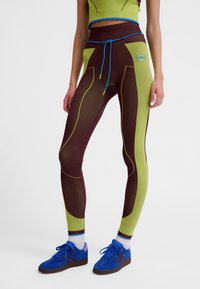 Tætsiddende leggings i grøn og bordeaux med ribbet tekstur, kontrastfarvede sømme og en blå snor i taljen.