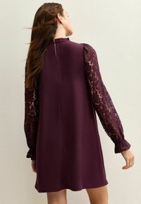 Vestido burdeos con mangas largas de encaje, puños fruncidos y cuello alto. Tela lisa con detalles de encaje en las mangas.