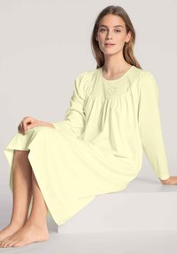 Camicia da notte a maniche lunghe di un delicato giallo chiaro, realizzata in tessuto morbido, con una scollatura arricciata e un delicato ricamo sul petto.