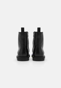 Las botas de tobillo de cuero negro presentan un acabado suave, cremalleras laterales y pestañas de tela. Las suelas son planas con un diseño minimalista.