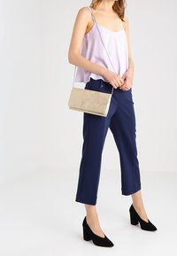 Světle fialová košilka, tmavě modré kalhoty do poloviny lýtek, černé lodičky na vysokém podpatku a zlatá kovová kabelka s řetízkovým popruhem. Celkově hladká textura.