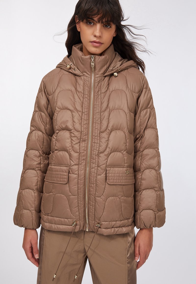 Giacca a piumino marrone trapuntata con colletto alto, chiusura con zip e due tasche frontali. Presenta coulisse all'orlo e una texture del tessuto lucida.