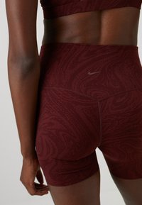 Burgunder fargede treningsshorts med et teksturert mønster med sirkulære og bølgete design, laget av elastisk stoff for komfort.