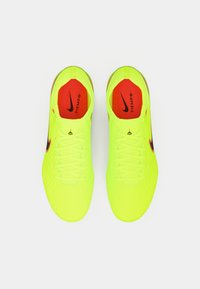 Gule syntetiske fodboldstøvler med struktureret overflade, flade snørebånd, røde indlægssåler og sorte Nike-logo akcenter. Designet til præstation.