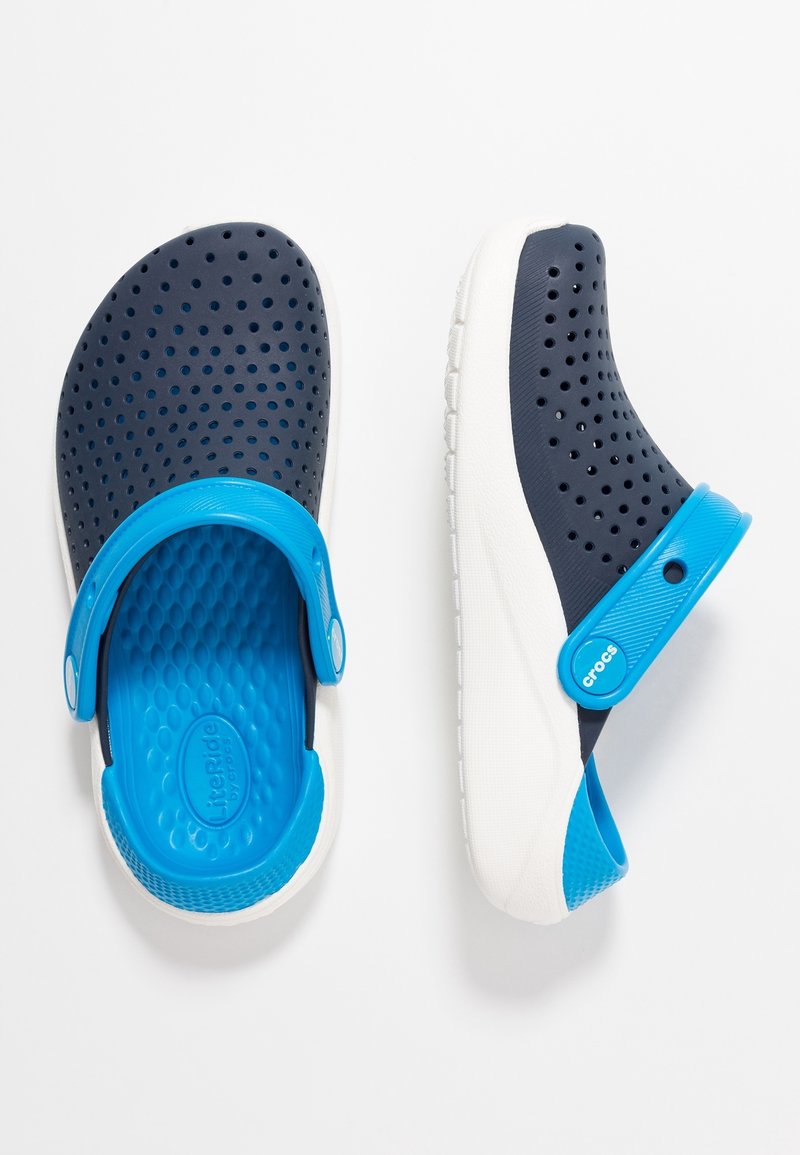 Paire de sabots bleu marine et bleu brillant avec empeignes perforées et semelles blanches, positionnés avec une chaussure retournée et l'autre en vue latérale.