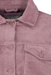 Růžová manšestrová bunda s špičatým límečkem, dvěma knoflíky a náprsní kapsou s klopou. Textura je jemná a ribbovaná.