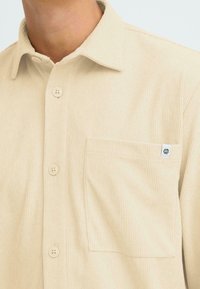 Bežist kordurooheline särk terava kraega, nööbkinnise ja rinnataskuga, millel on väike logopatch taskul.