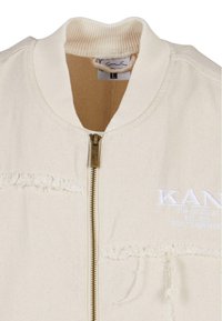 Off-white bomberjakke med ribbestrikket krage, gullglidelås, frynsete detaljer og brodert logo. Laget av teksturert stoff med lommer.