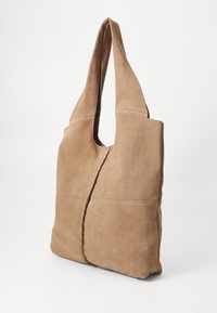 Sac fourre-tout en cuir suédé brun avec une forme de hobo, doté d'une seule poignée et d'une couture décorative le long des coutures. Texture lisse et design minimal.