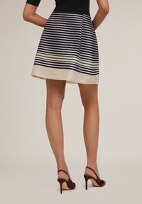 Striped skirt in navy and cream, pleated design, with a satin finish and a hem lined in cream. Worn with burgundy slingback heels.