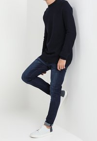 Marinblå stickad tröja, slim fit mörka jeans och vita sneakers med grå detaljer. Outfiten har en texturerad finish och en avslappnad passform.