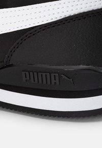 Schwarze Sneakers mit einem strukturierten Lederoberteil, schwarzen und weißen Akzenten, auffälligem PUMA-Logo und einer Gummisohle mit weißem Streifen.