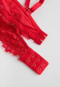Red bra featuring lace trim, smooth fabric, adjustable straps, and gold-tone hardware on the hook-and-eye closure.