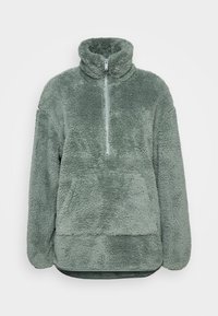 Pulower z imitacji futra w jasnej zieleni, z wysokim kołnierzem i suwakiem do połowy długości. Miękka tekstura i luźny krój. Pozioma szew w talii.